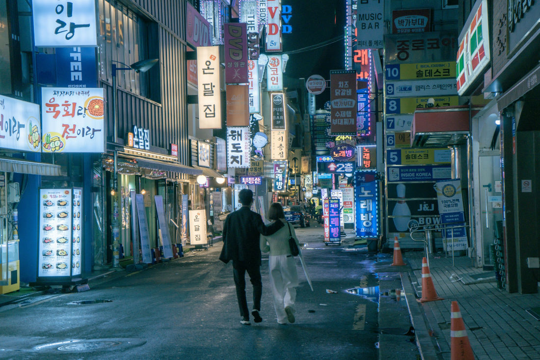 An nighttime image of a couple walking on a street in Seoul