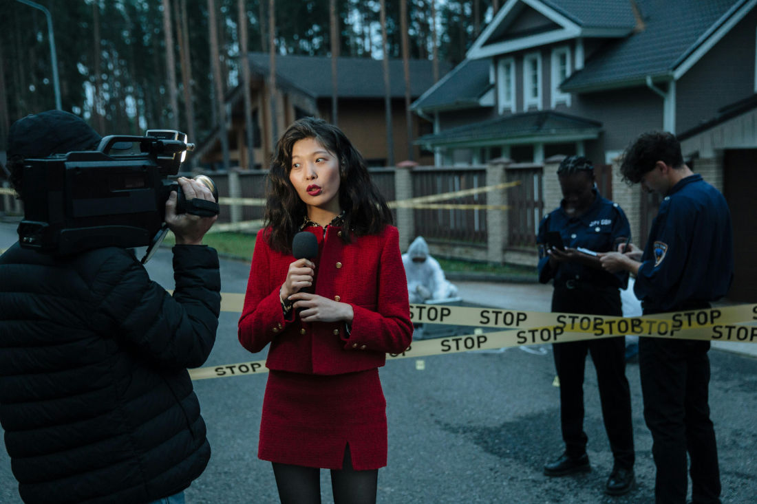 A reporter covering a crime scene for a TV news station with police in the background